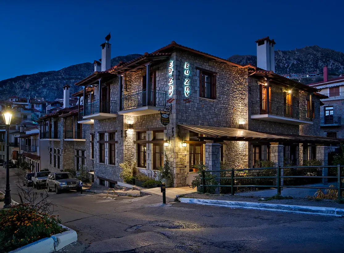 Πέτρινο ξενοδοχείο τη νύχτα με φωτισμένη πινακίδα και μπαλκόνια
