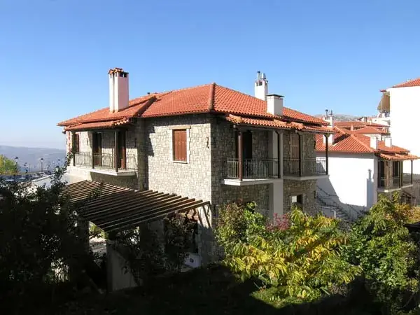 Πέτρινο κτίριο με κεραμοσκεπή και μπαλκόνια μέσα σε πράσινο